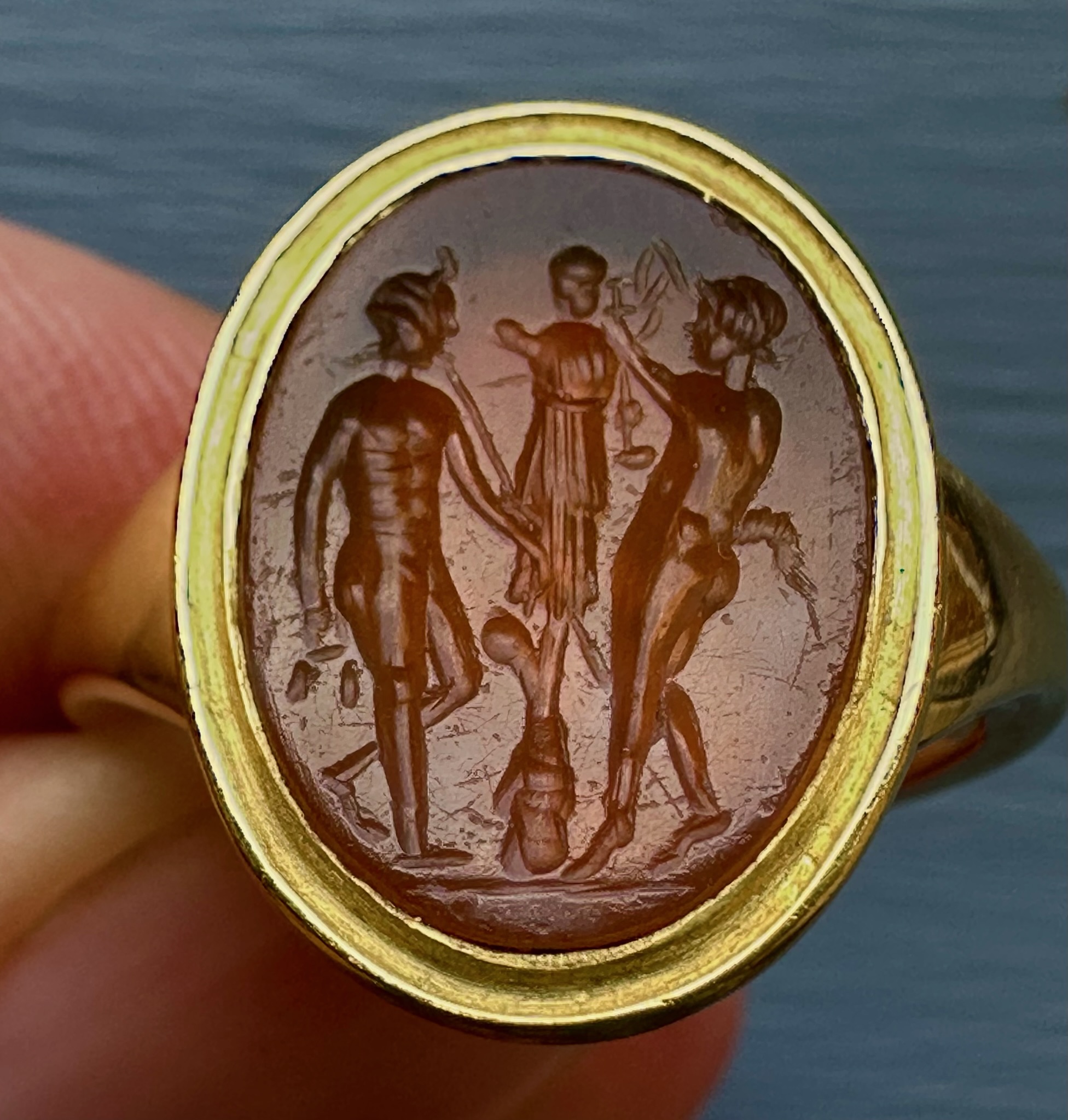A gold ring set with a Roman Carnelian intaglio. Two Satyres crowning a trophy