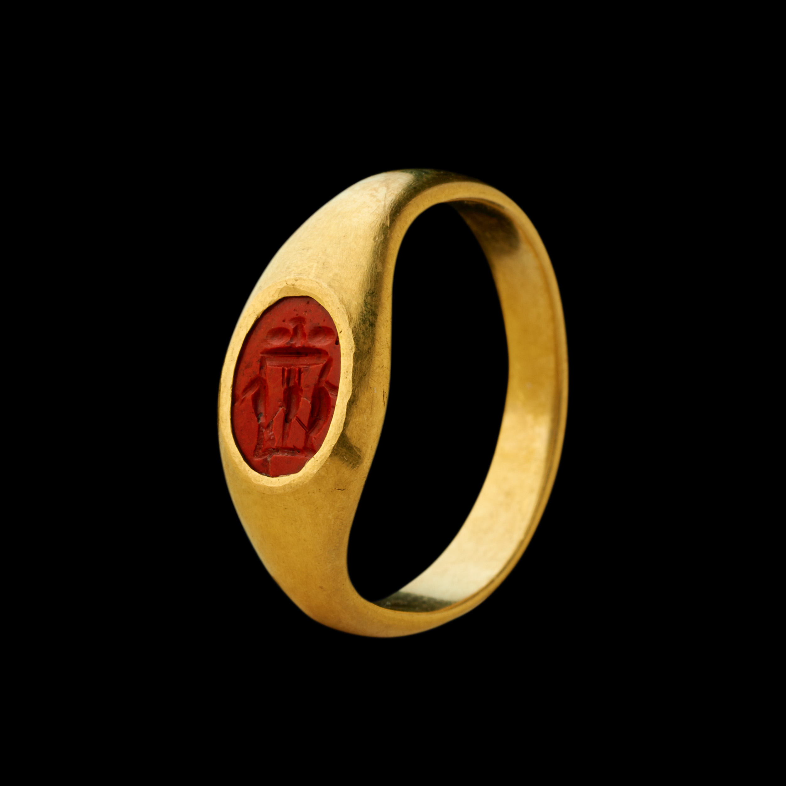 Intaille romaine en jaspe rouge montée sur une bague en or à haut titre. Table à trois pieds chargée de vases.