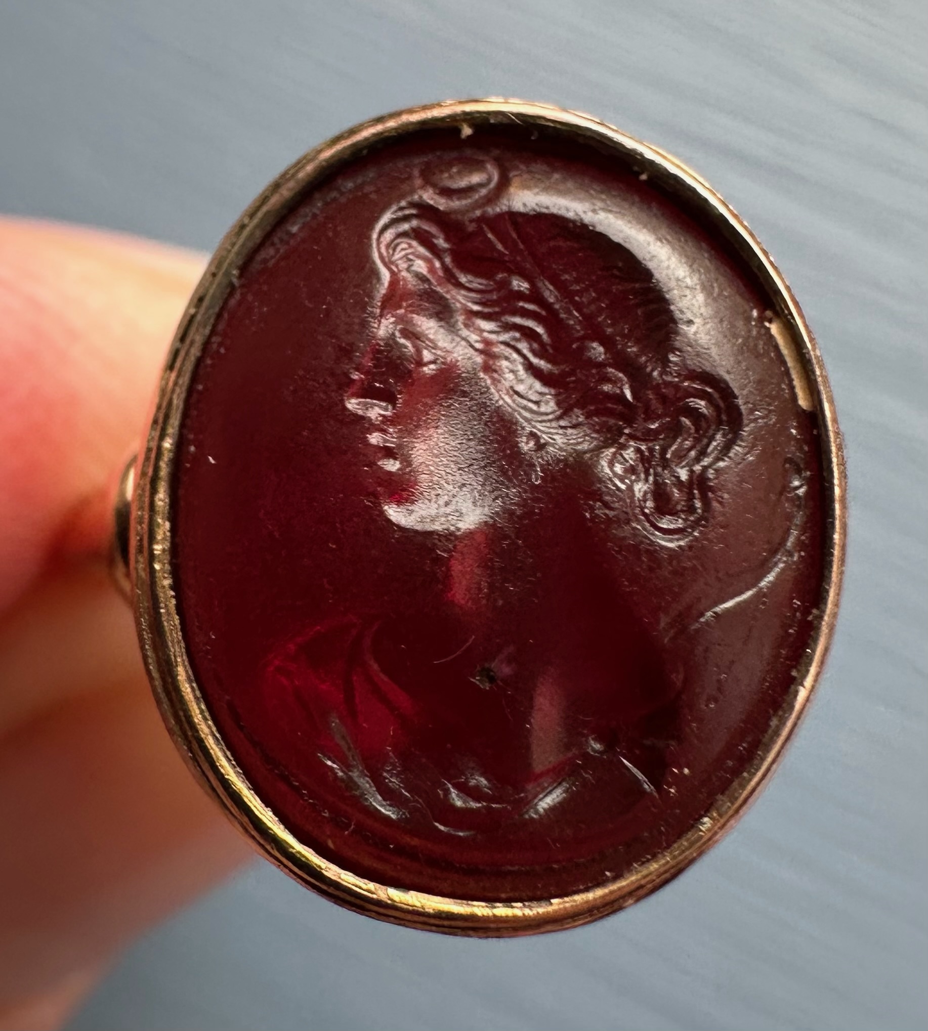 A gold ring set with a 19th century red glass intaglio. Bust of Diana.