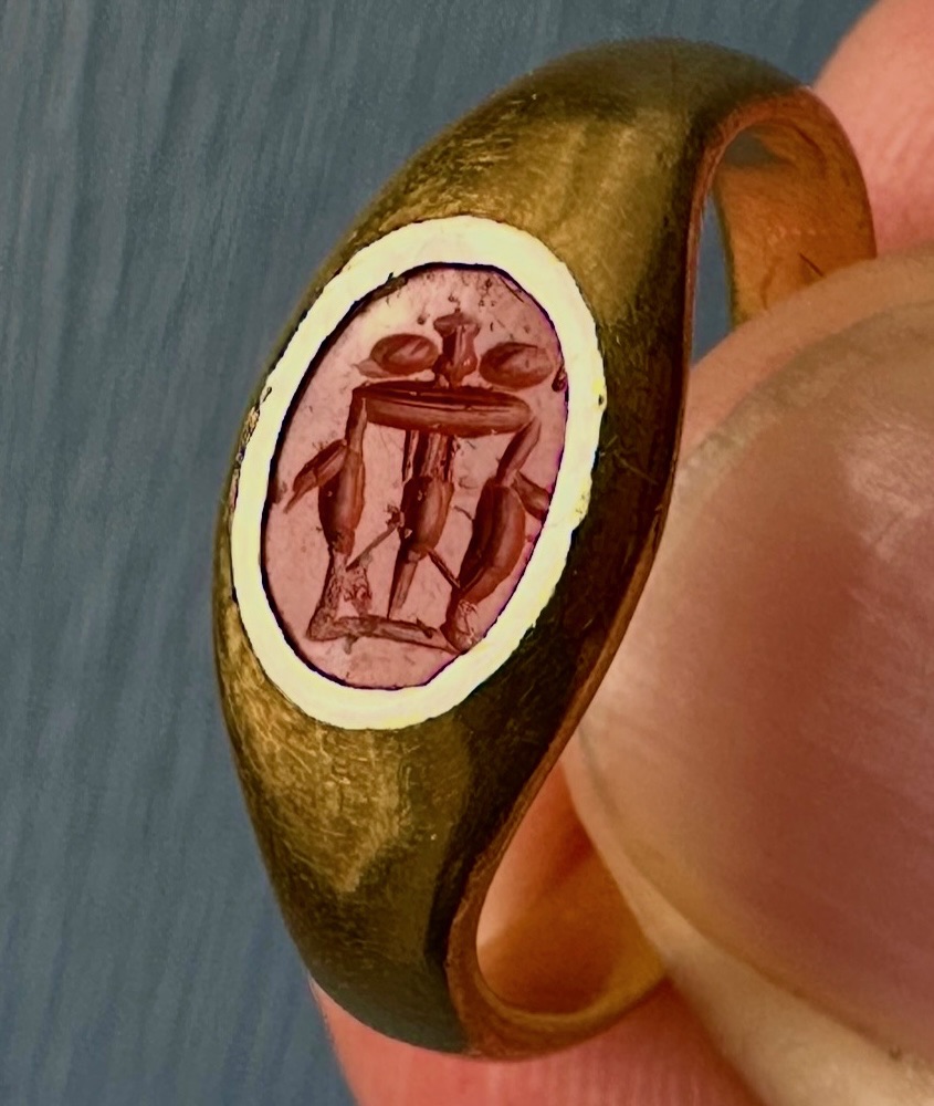 Intaille romaine en jaspe rouge montée sur une bague en or à haut titre. Table à trois pieds chargée de vases.